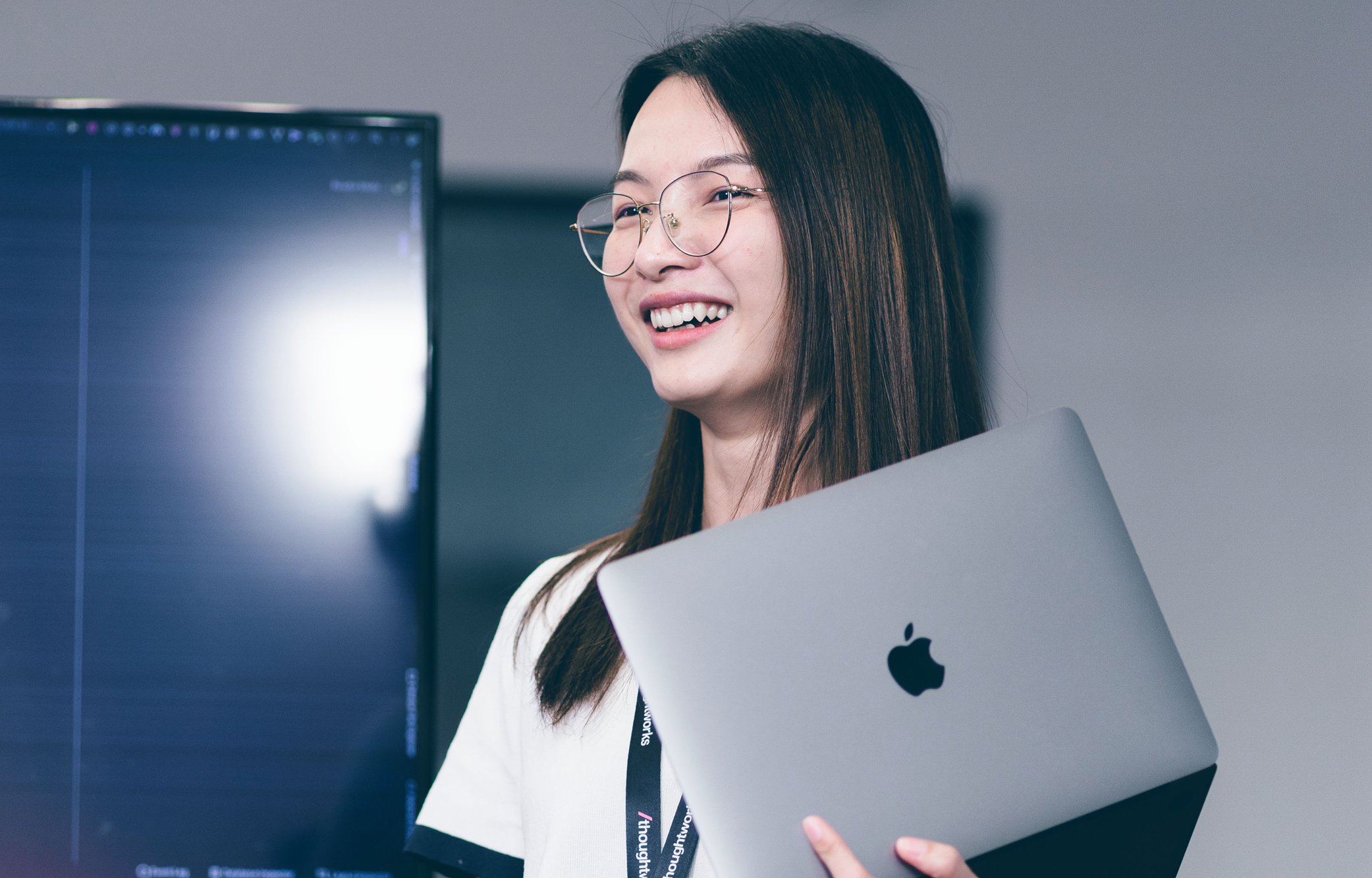 Image of a Thoughtworker smiling at the camera while holding a MacBook.