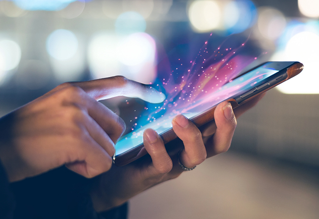 Close-up of someone using a mobile phone. The screen of the phone is emitting rays of light.
